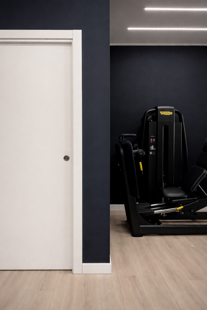 Palestra FITLAB Reggio Calabria – Realizzato: dettaglio sala macchine con attrezzatura Technogym e contrasto porta bianca su parete antracite